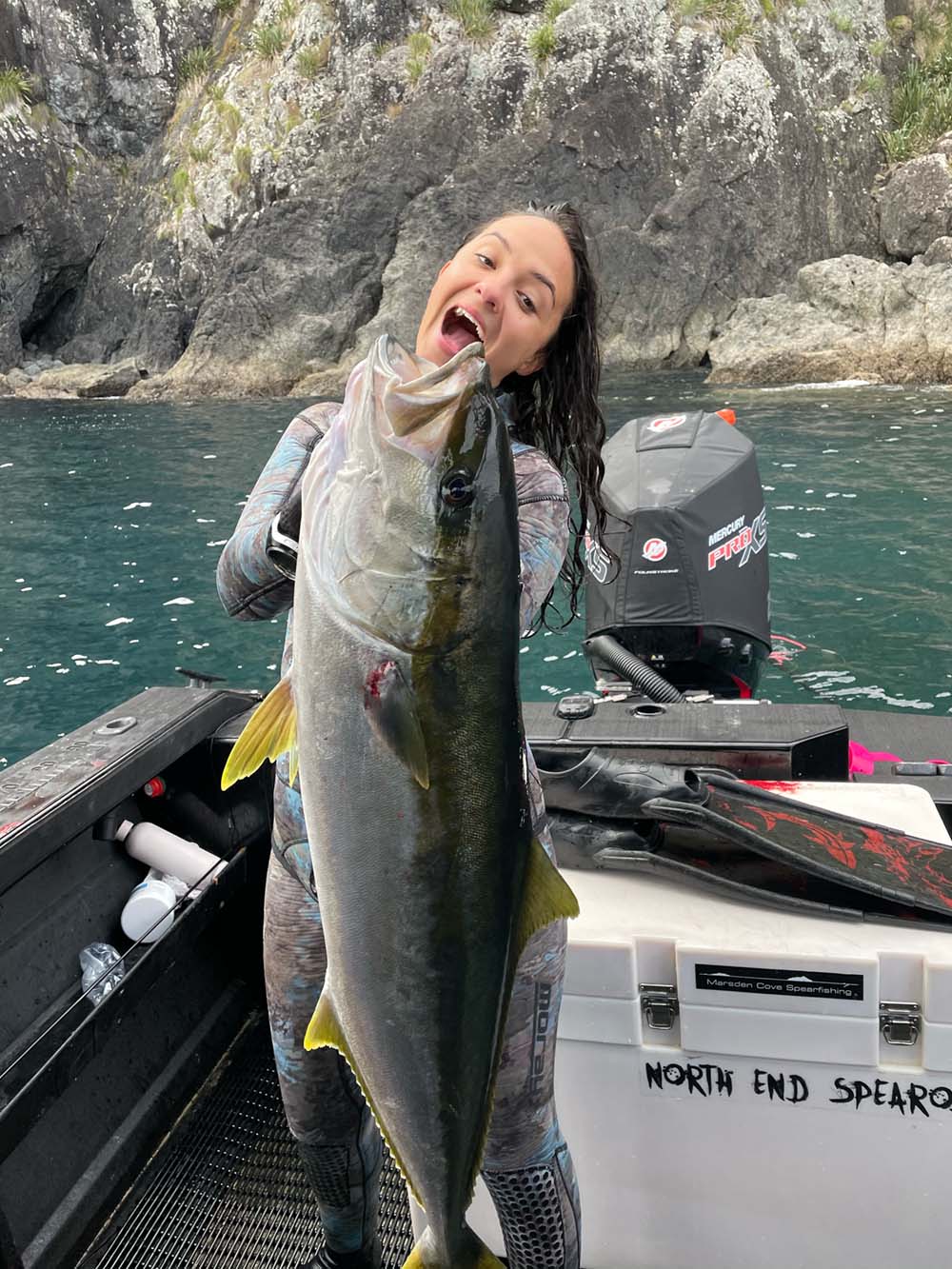 Renee holding a large fish on a boat with rocky cliffs in the background
