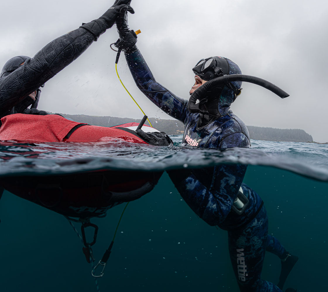 Two free divers giving a high-five underwater with a kayak in the background.