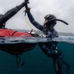 Two free divers giving a high-five underwater with a kayak in the background.