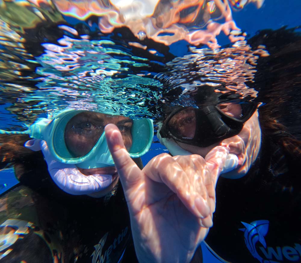 Two snorkelers underwater with bubbles and clear blue water.