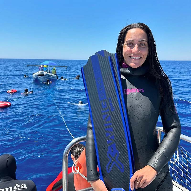 Benny in a wetsuit holding fins on a boat with blue water and clear sky