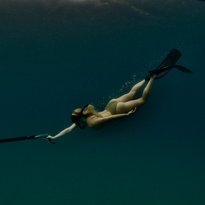 Camille free diving in deep blue water with speargun