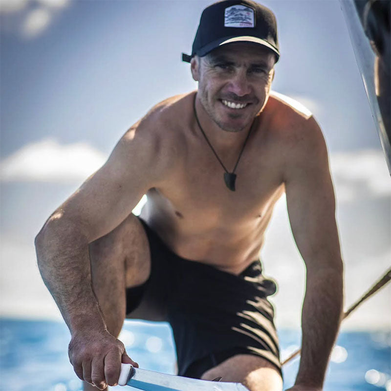 Jules on a boat wearing a cap and black shorts, with water and sky in the background
