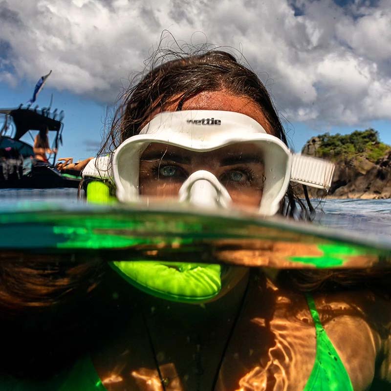 Laura snorkeling with a mask and snorkel, underwater view with boat and rocks in the background