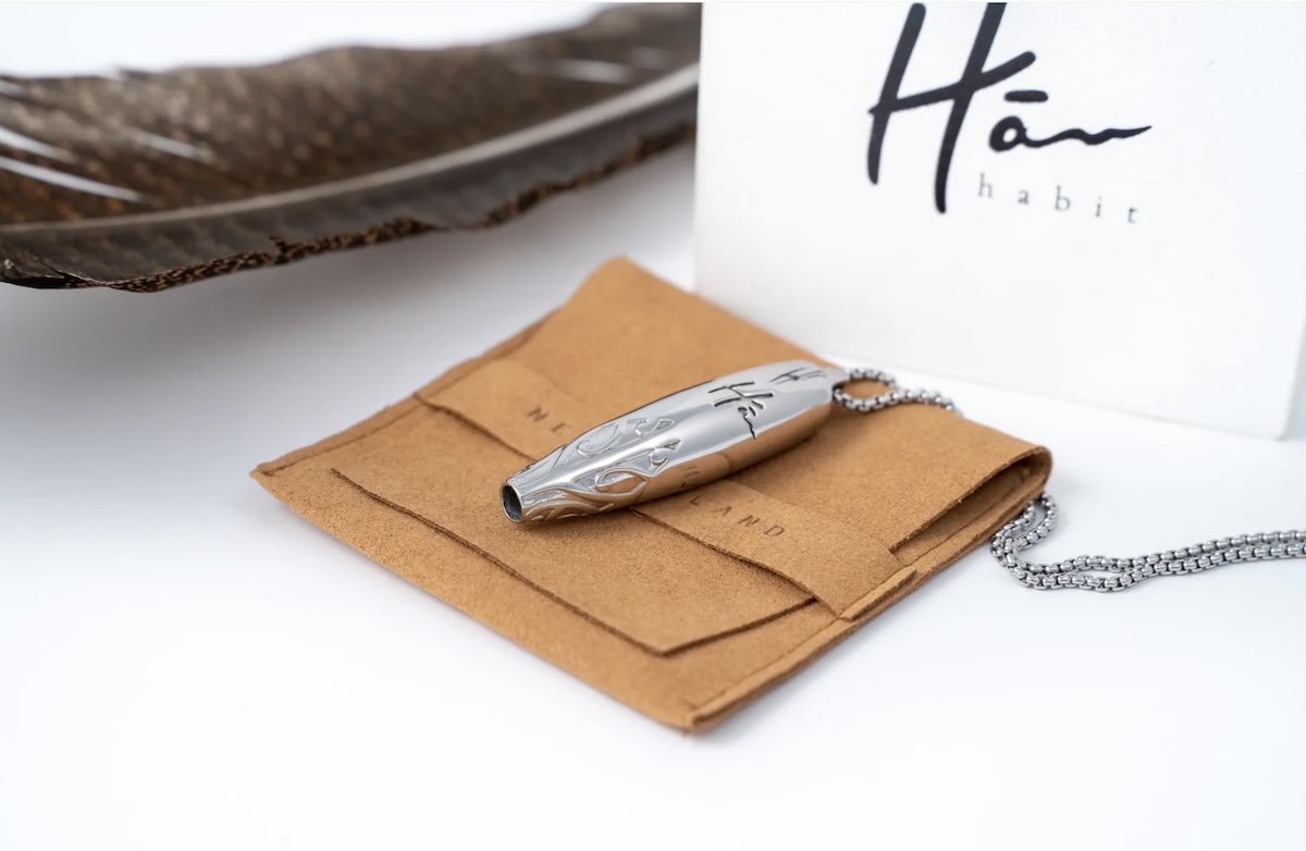 Silver necklace with a feather on a white background, featuring the brand 'Hā'.
